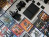 Addio al supporto fisico: cosa resta dei videogiochi? Una console PlayStation 2 nera e i suoi accessori disposti su una superficie chiara, circondati da numerose custodie di videogiochi originali
