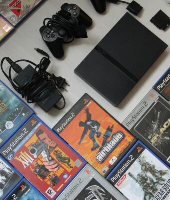 Addio al supporto fisico: cosa resta dei videogiochi? Una console PlayStation 2 nera e i suoi accessori disposti su una superficie chiara, circondati da numerose custodie di videogiochi originali
